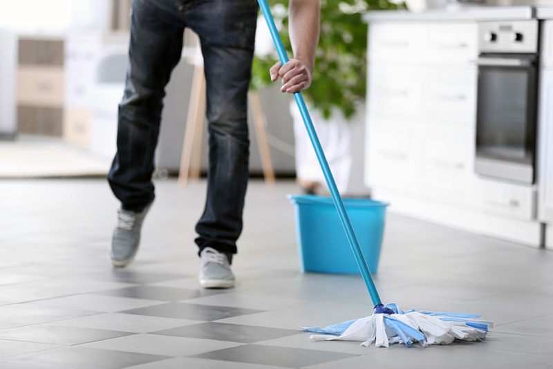 یک نظافتچی در حال نظافت و تی کشیدن کف آشپزخانه منزل