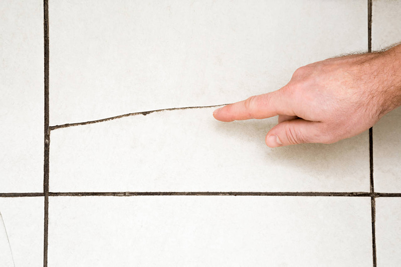 دستی در حال اشاره به ترک ایجاد شده روی سرامیک کف خانه