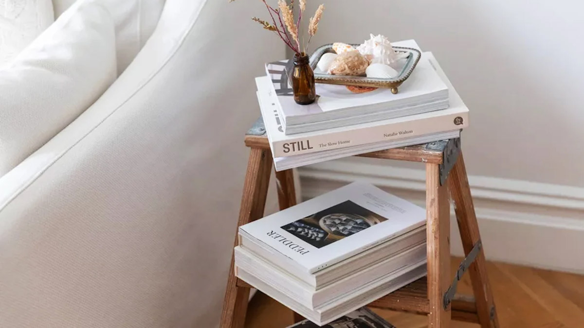 تعدادی کتاب روی میز کنار مبل که با استفاده از دو نردبان دکوری ساخته شده