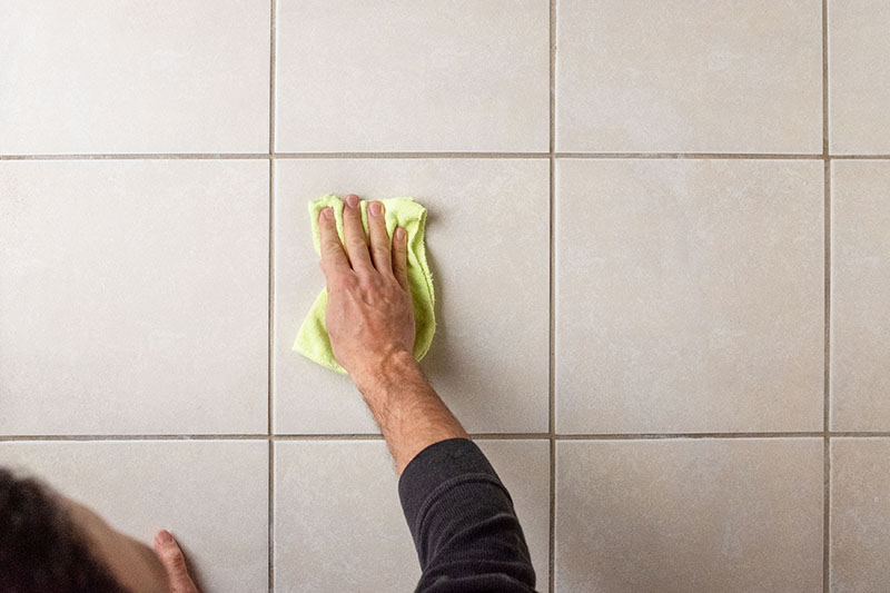 فردی در حال تمیز کردن سرامیک کف با دستمال پارچه‌ای