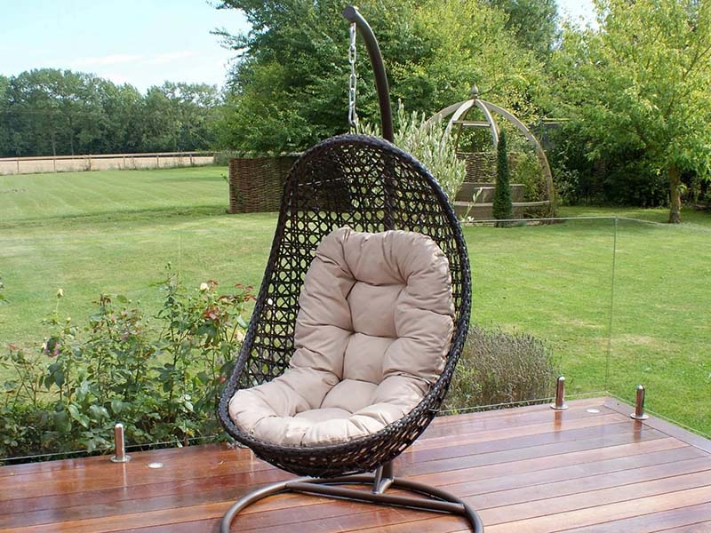 یک صندلی تابی روی تراس چوبی در یک باغ