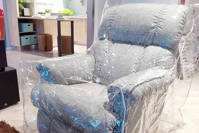 یک کاناپه تک نفره طوسی که روی آن روکش پلاستیکی کشیده شده