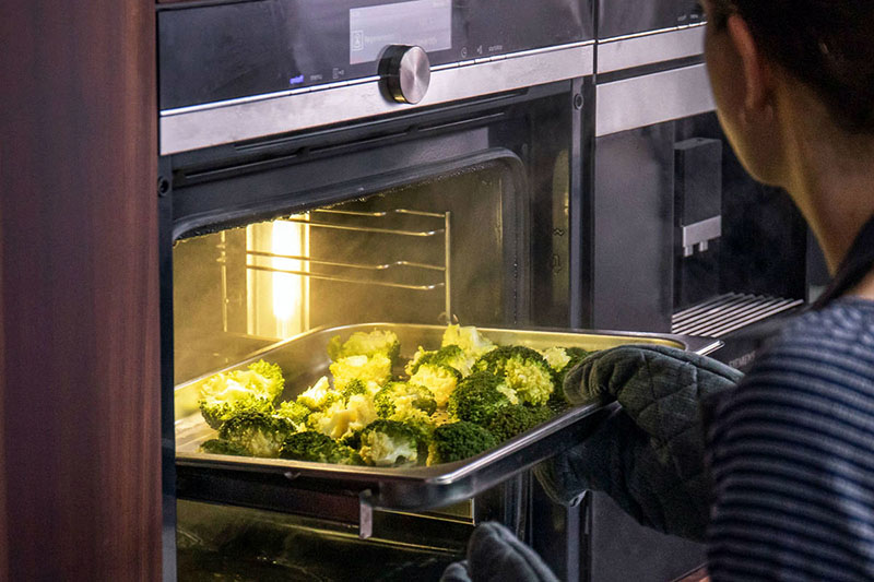 فردی در حال قرار دادن سینی سبزیجات داخل دستگاه بخارپز توکار