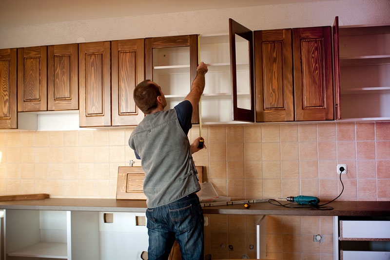 یک نجار در حال اندازه‌گیری طبقات کابینت چوبی با متر در آشپزخانه