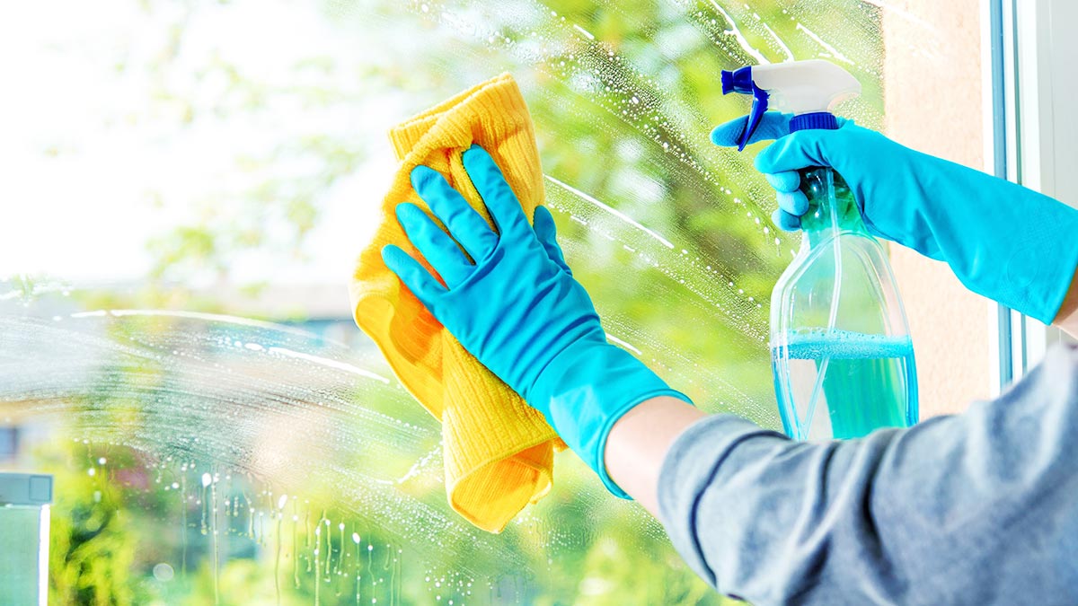 دستان فردی در حال تمیز کردن شیشه پنجره با دستمال و محلول شیشه‌شوی