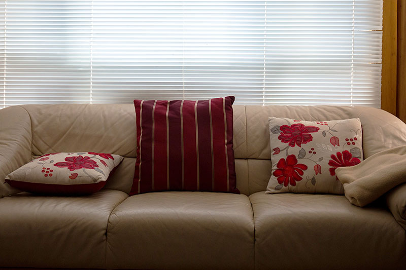دو کوسن گلدار و یک کوسن راه‌راه قرمز روی کاناپه چرمی کرم رنگ