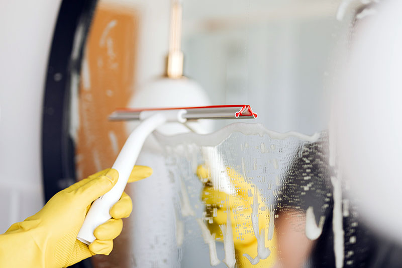 یک تی شیشه‌شوی در دست یک نظافتچی ساختمان در حال تمیز کردن آینه